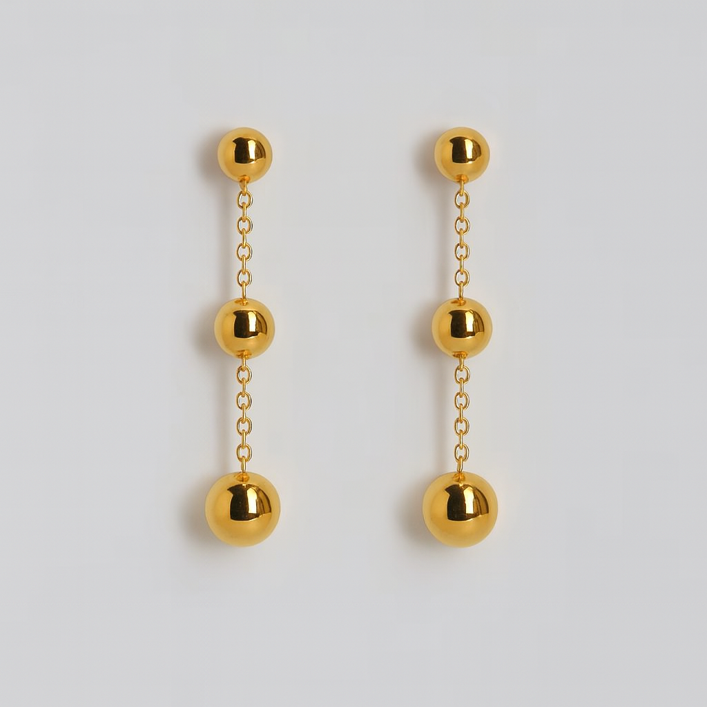 Gold ball drop earrings on a light gray background