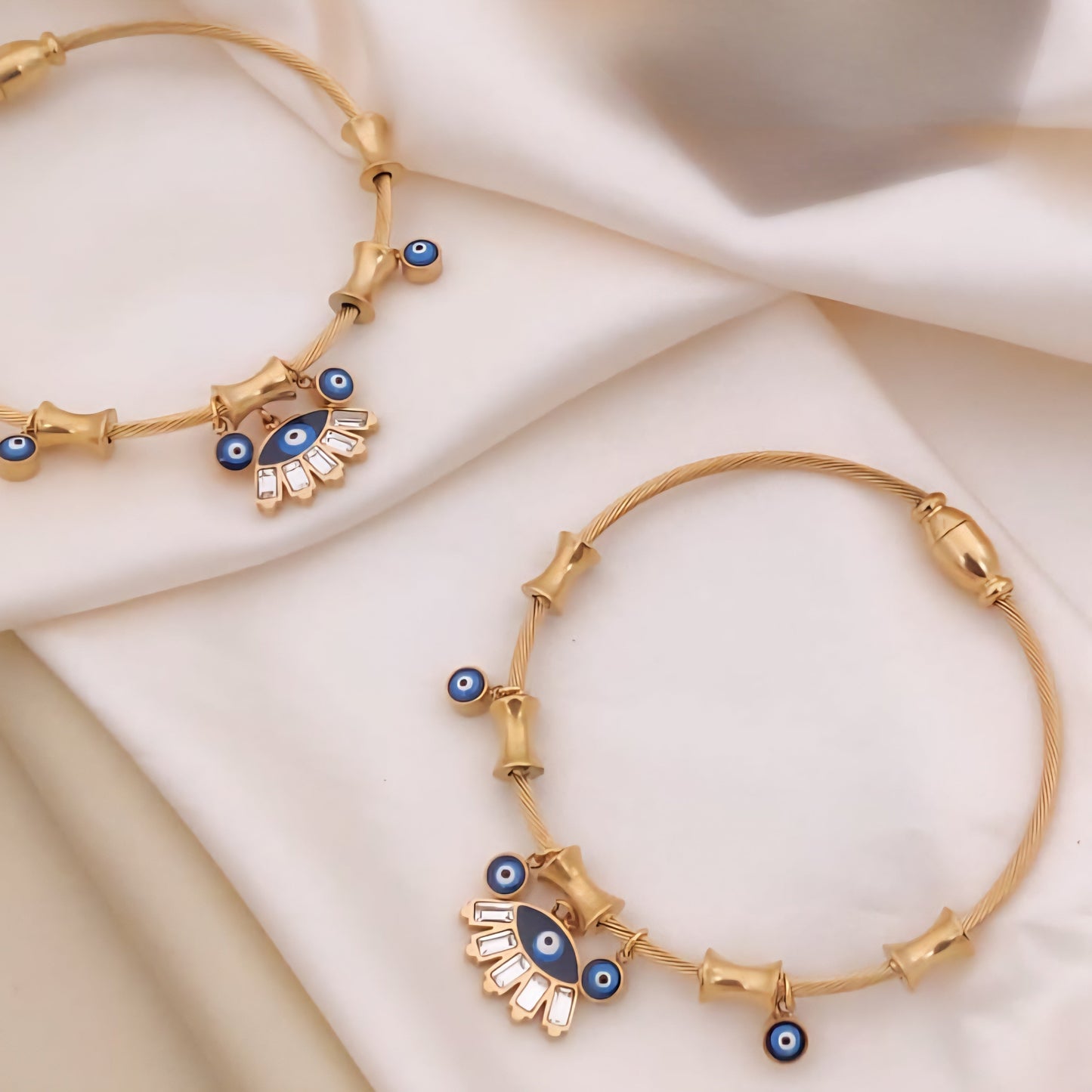 Gold bracelets with blue eye designs on a beige fabric background
