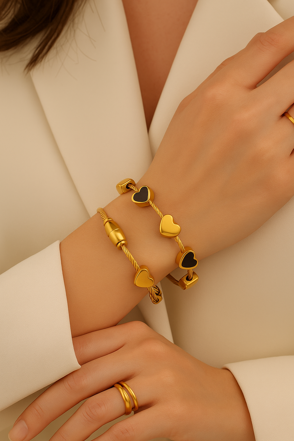 Gold bracelets with heart charms on a person wearing a white blazer.
