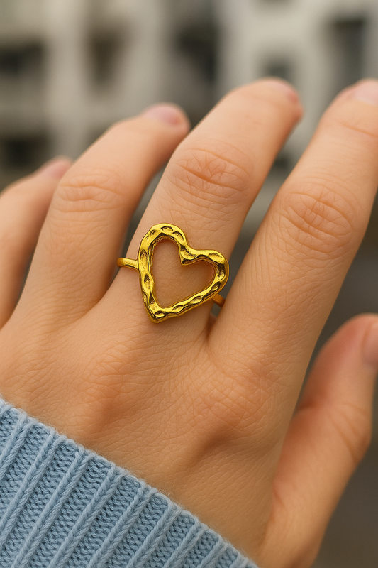Gold heart-shaped ring on a person's finger with a blurred background