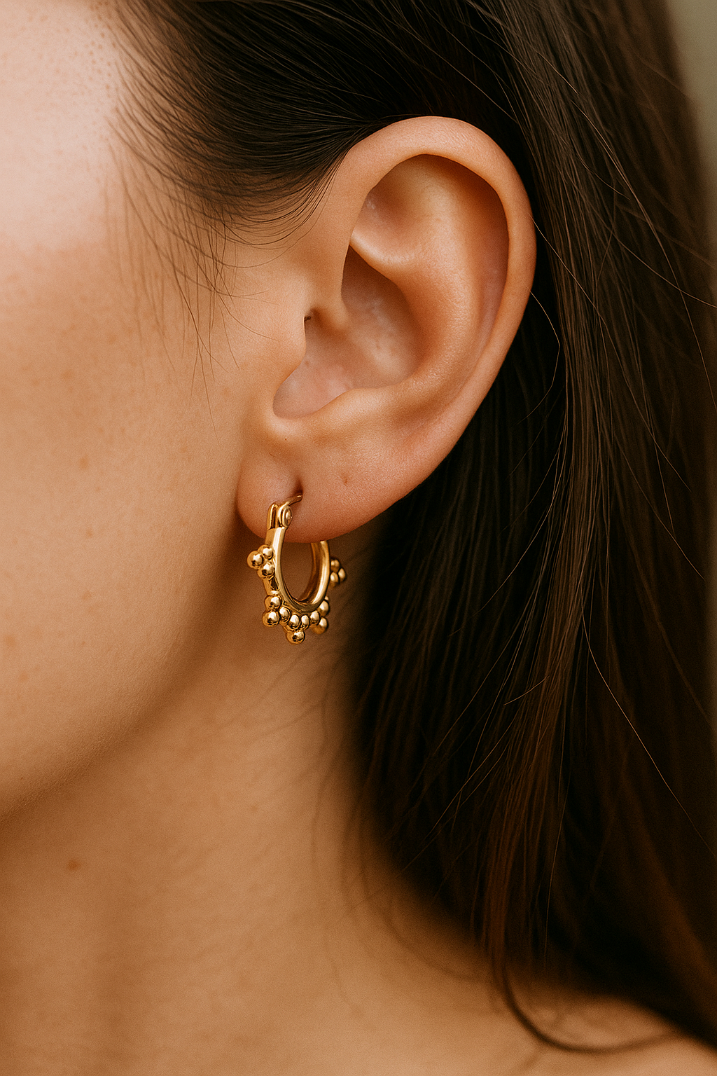 Close-up of an ear wearing a gold hoop earring with small beads.