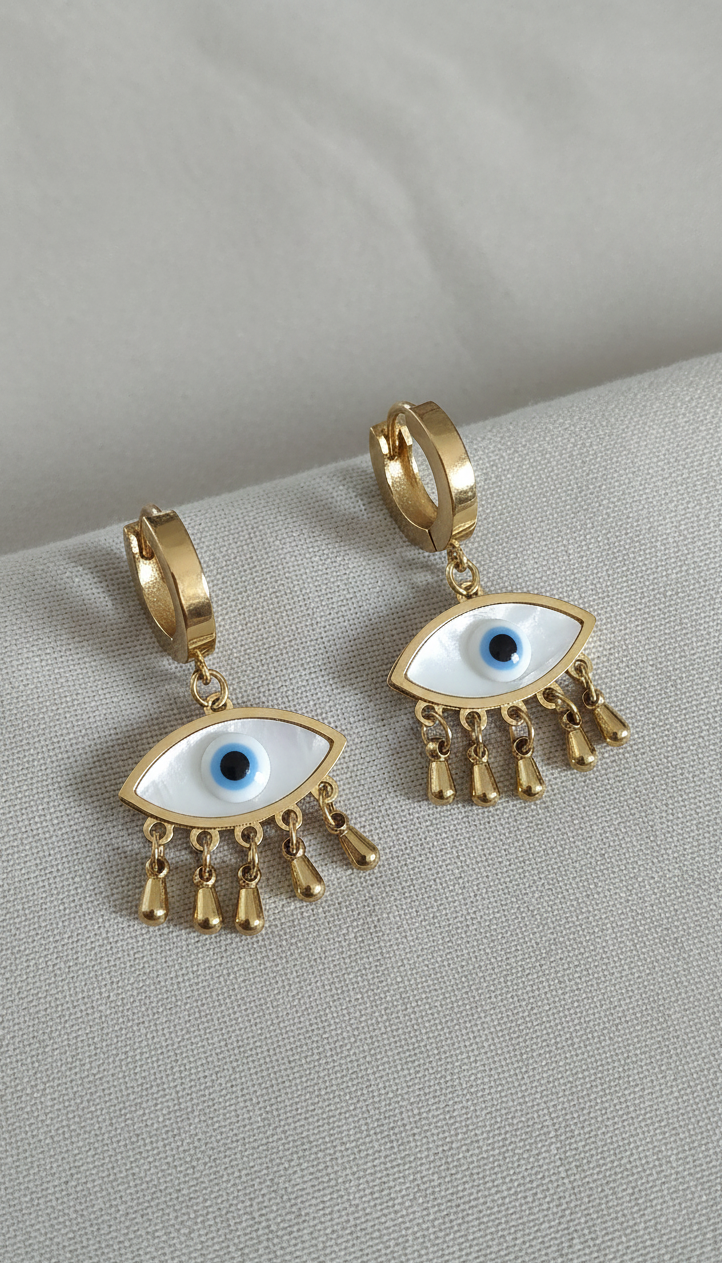 Gold hoop earrings with eye-shaped charms on a gray surface