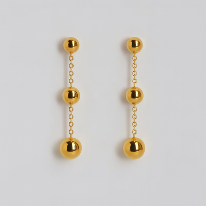 Gold ball drop earrings on a light gray background

