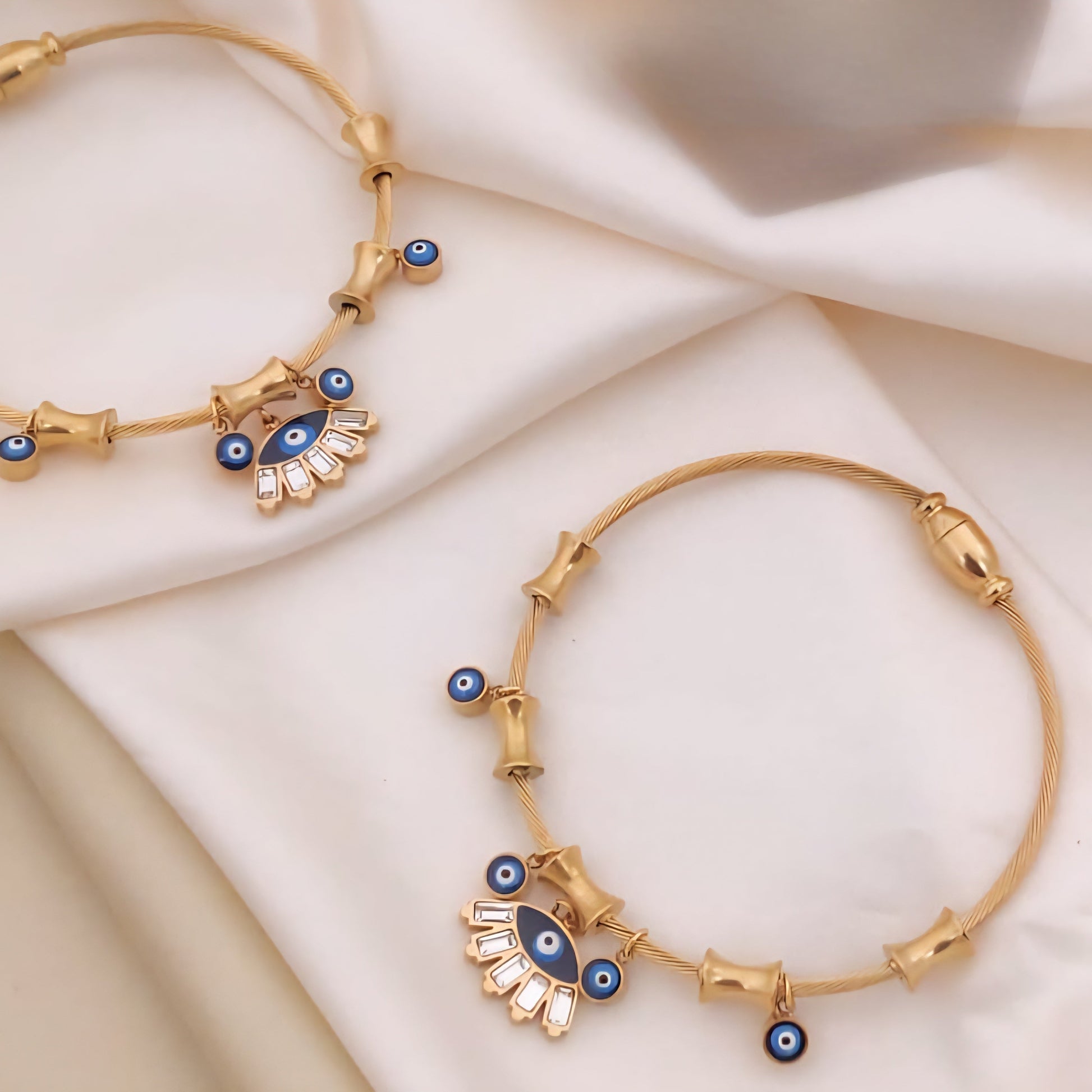 Gold bracelets with blue eye designs on a beige fabric background

